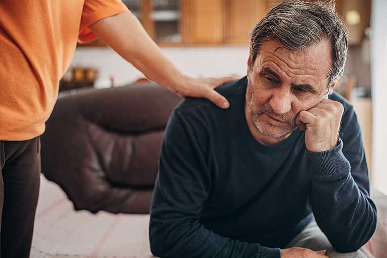 Older man unshaven and feeling down with supportive hand on his shoulder